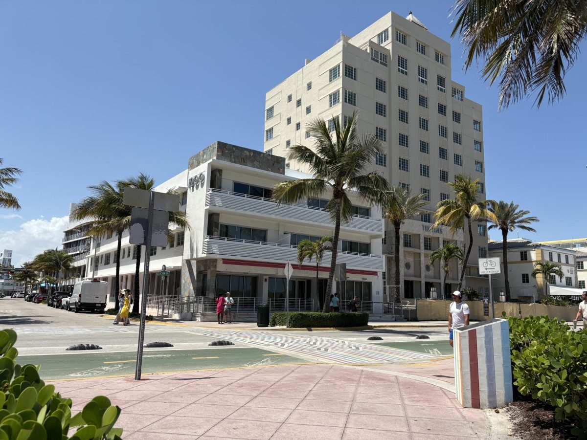 Pedestrians stroll along a vibrant crosswalk at the intersection of Ocean Drive and 12th Street, located in Miami Beach, Florida. Photographed during a sunny day on April 11th, 2025, this scene features iconic Art Deco themed buildings, such as the 10-story Tides Hotel and the 1220 Ocean Drive structure. 